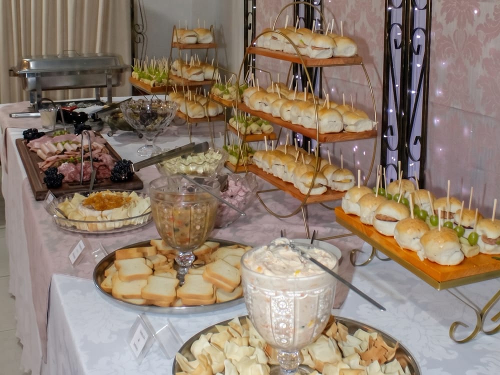 Mesa de entradinhas do buffet com mini sanduíches, tábua de frios, torradas e patês
